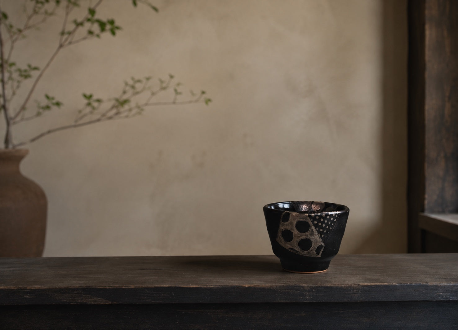 A dark Japanese cup placed quietly on a wooden table near soft window light